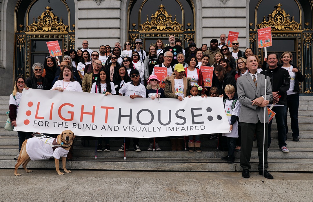 LightHouse staff, students, and supports stand outside San Francisco City Hall holding a LightHouse banner