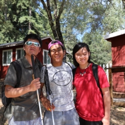 Three teens stand together in front of the lakeside cabins at camp
