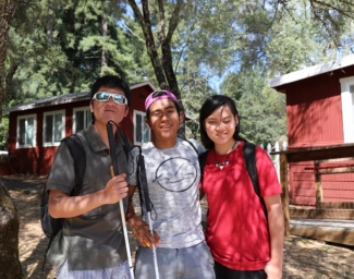 Three teens stand together in front of the lakeside cabins at camp