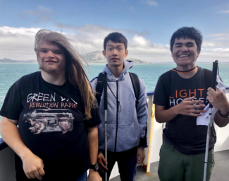 Three Yes Academy Students on a Ferry with their White Canes, looking at the camera and smiling.