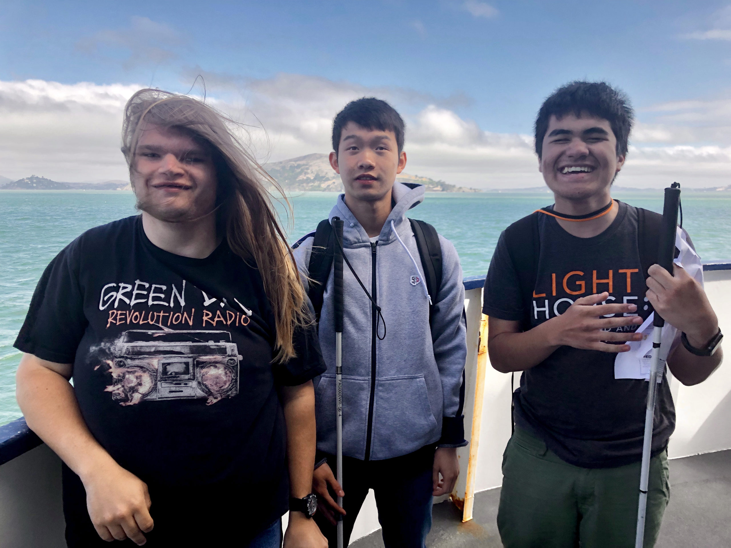 Three Yes Academy Students on a Ferry with their White Canes, looking at the camera and smiling.