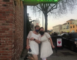 Two people wearing white dresses, masks and running shoes pose for a photo