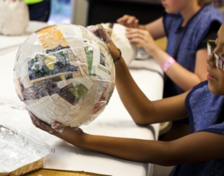 A child holds a balloon covered in papier-mâché at a previous Enchanted Hills Camp session