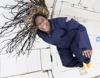 A woman wearing a navy blue spacesuit in a zero gravity environment. She has a big smile, her body is floating, and her hair is floating around her