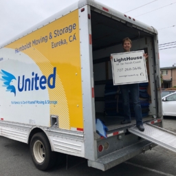 Janet Pomeranz standing in the opening of the Humboldt Moving and Storage Co. van holding a sign that says LightHouse of the North Coast