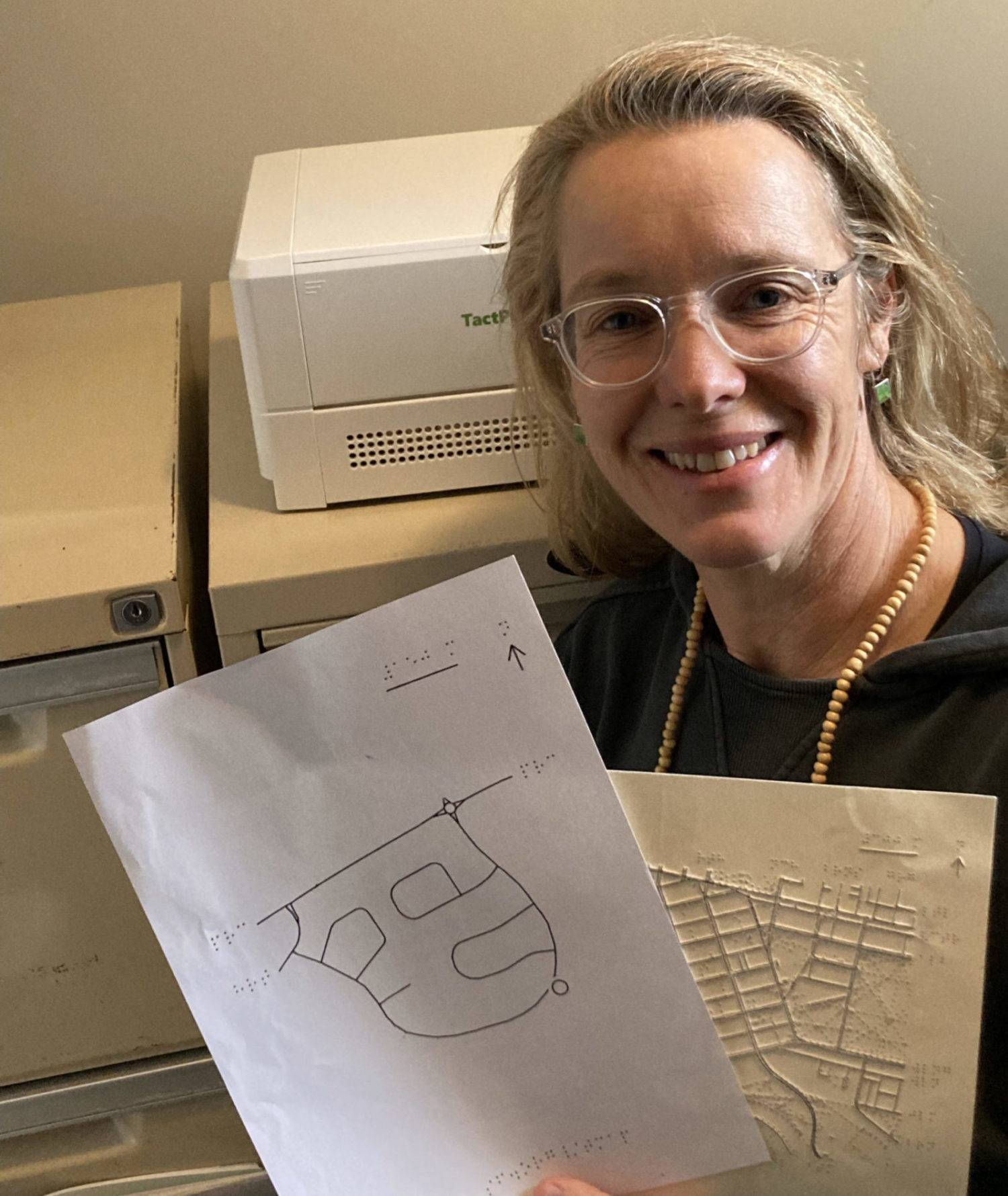 Orientation and Mobility specialist, Anegla Reynolds, poses with two TMAPs she has embossed for clients in Australia