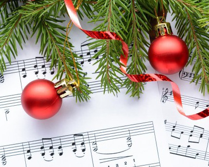 An image of sheet music, red ribbon, a red ornament, and pine tree branches