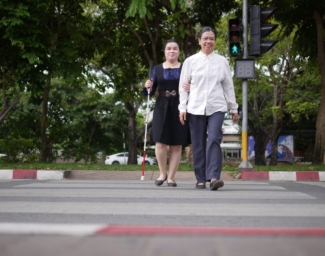 Two people cross an intersection with an APS. One is using a white cane