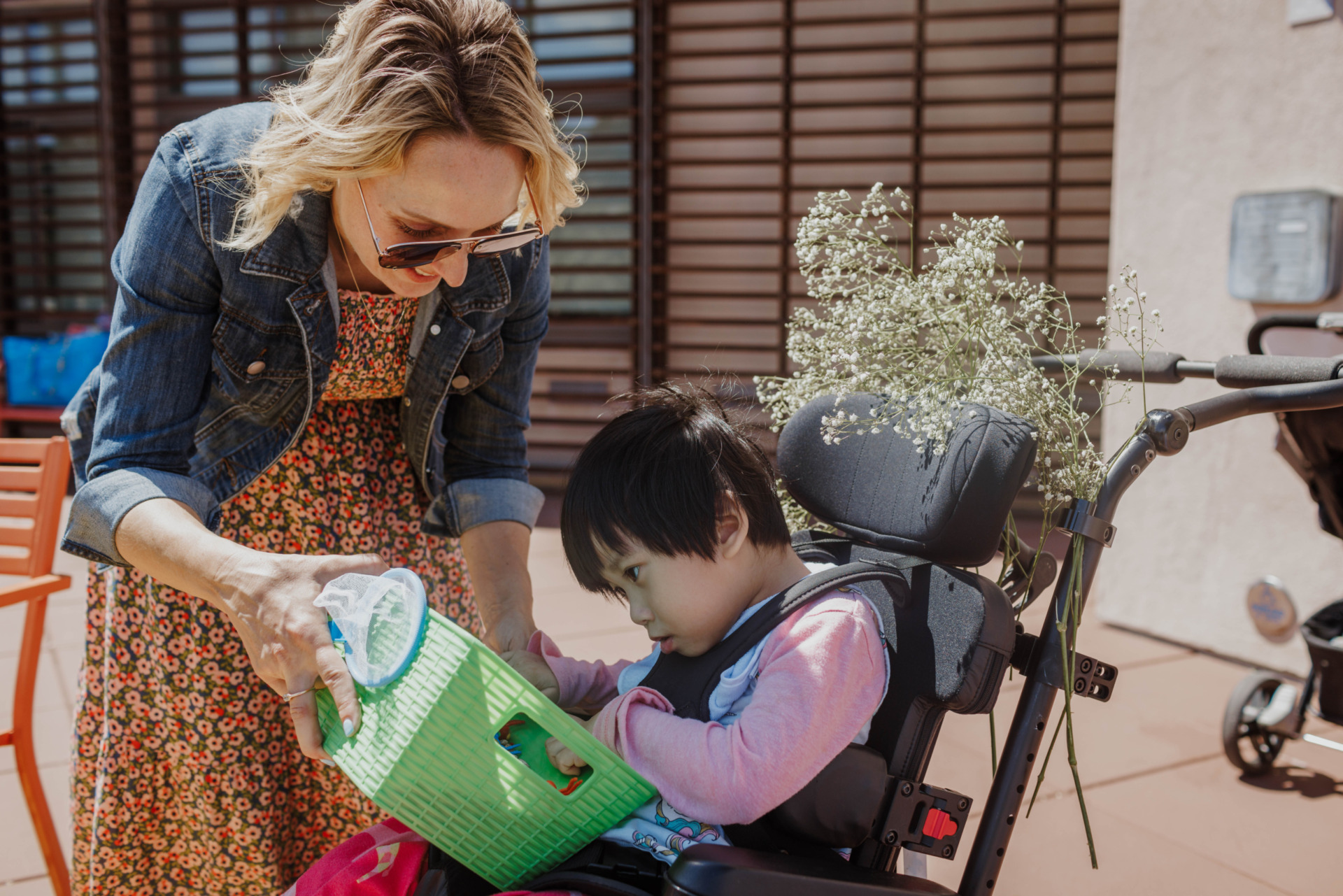 LightHouse Little Learners Specialist, Elizabeth, holds a sensory activity tray filled with beans and colorful plastic bugs for a little girl who is a wheelchair user