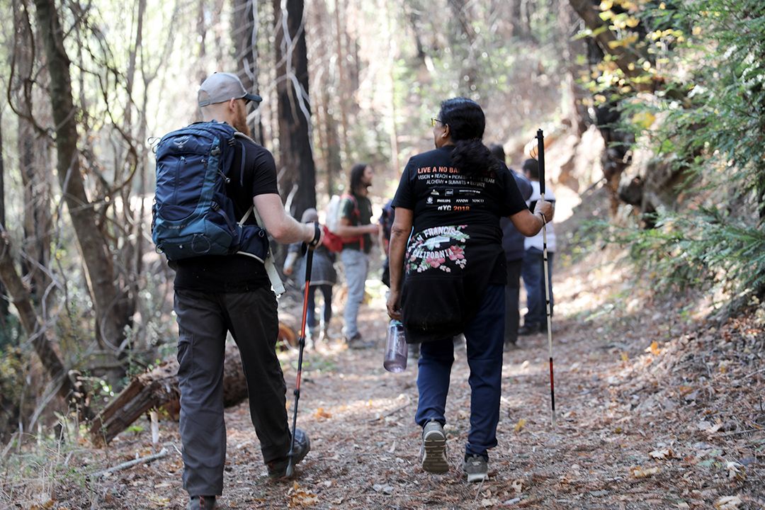A group of people with white canes hike a trail at Enchanted Hills Camp
