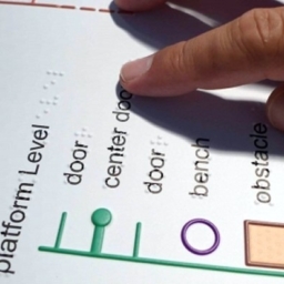 A closeup shot of a tactile BART Station map and a person reading the Braille labels with their fingers