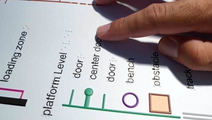 A closeup shot of a tactile BART Station map and a person reading the Braille labels with their fingers