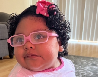Little Learners girl wears glasses with a pink frame and a pink bow in her hair