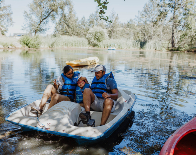 Little Learner sits between Shruti and adult family member on a paddle boat in the water