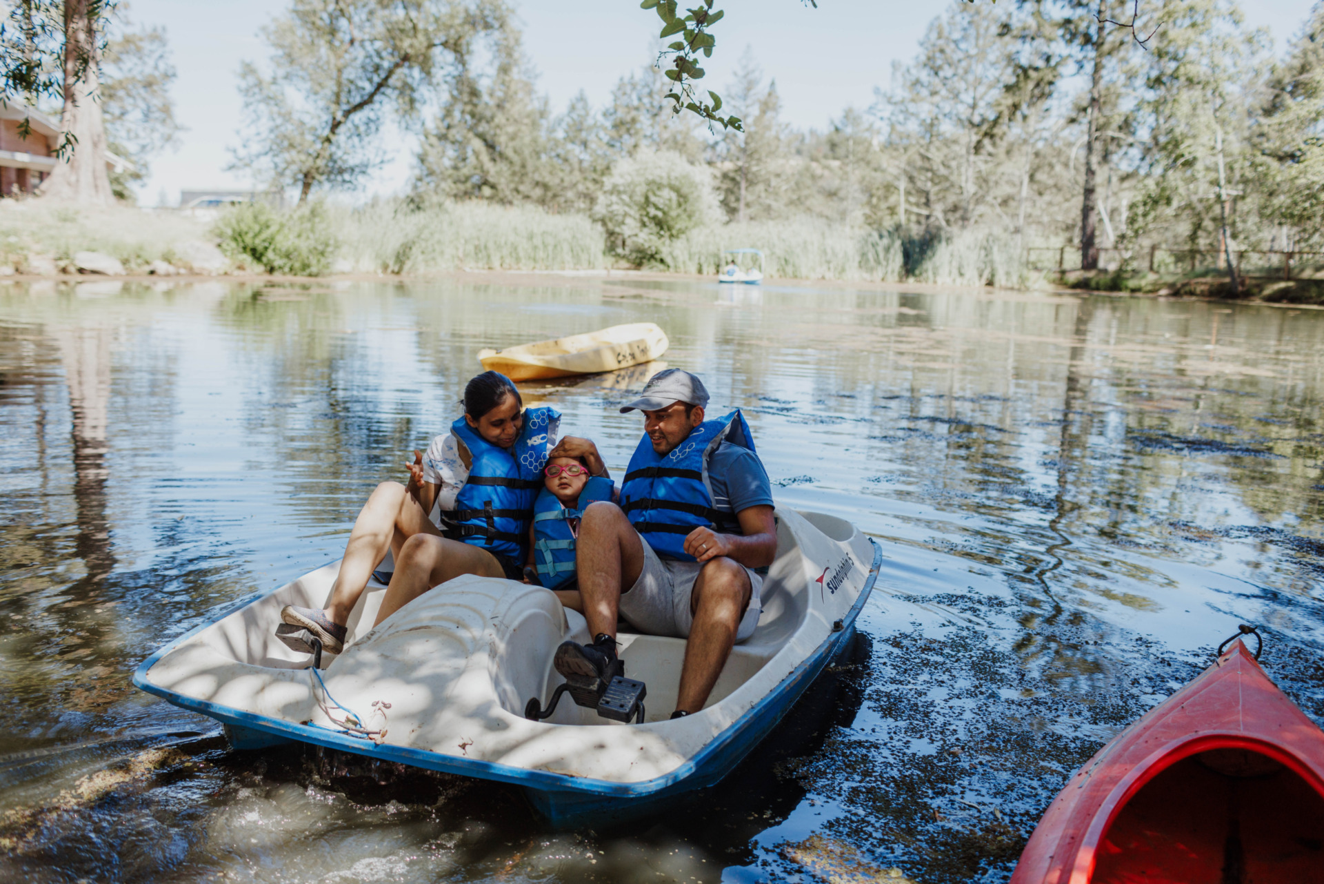 Little Learner sits between Shruti and adult family member on a paddle boat in the water