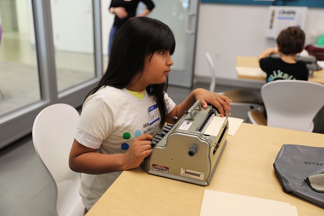 A child reads Braille on a sheet of paper inside a Perkins Brailler