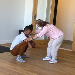 Improv Movement Gravity dancer, Gabrielle, Christian squats, and hold the hands of student Katlau, who bends over face-to-face and close up as they work together during and improvisational movement class.at LightHouse