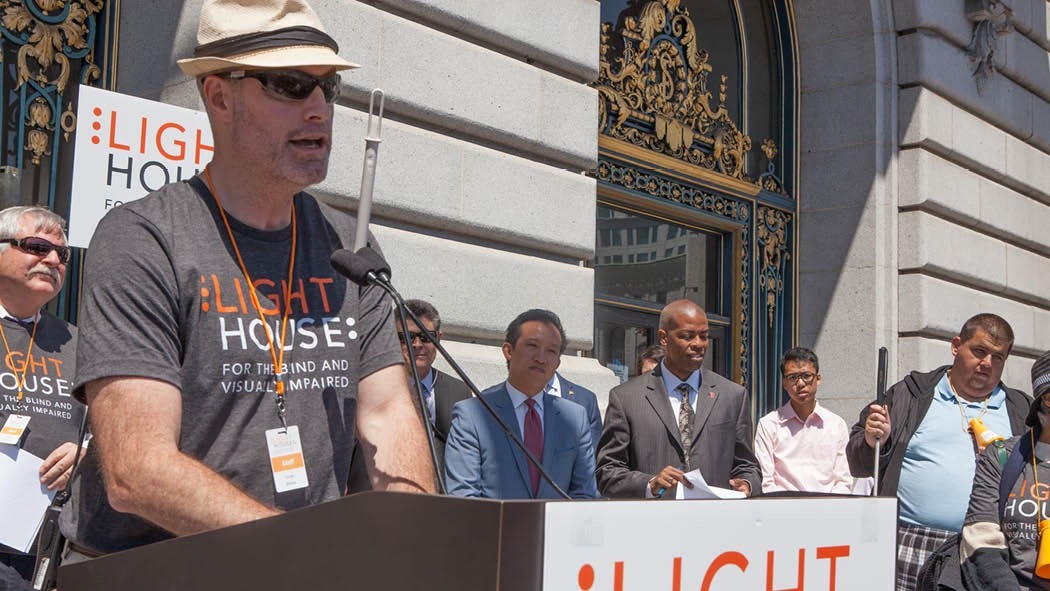LightHouse Vice President of Programs, Scott Blanks, stands at a podium on the steps of San Francisco City Hall as officials and LightHouse students look on at a previous LightHouse Day