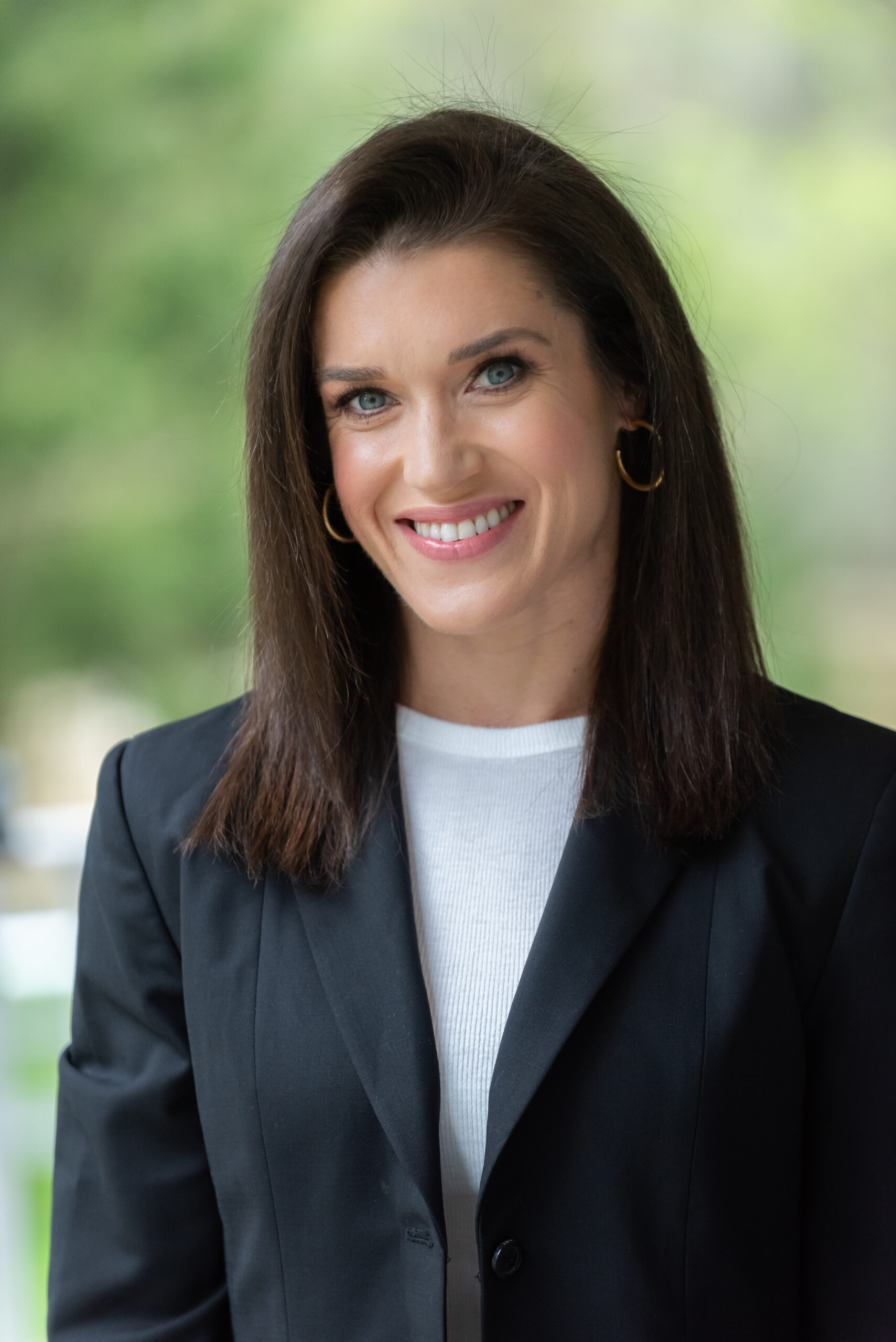 Rebecca Alexander is a woman with dark brown shoulder length hair and is wearing a white blouse under a black blazer.