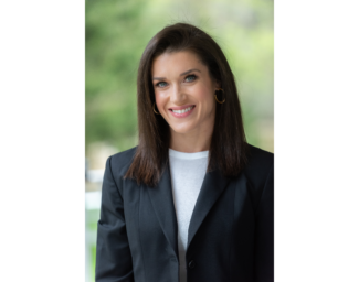 Rebecca Alexander is a woman with dark brown shoulder length hair and is wearing a white blouse under a black blazer.