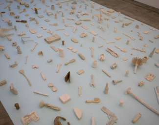 Clay replicas of everyday objects, made by Cara Levine, sit on a platform.