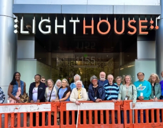 The June 2023 CVCL students and staff stand outside LightHouse headquarters. They are lined up behind an orange barricade