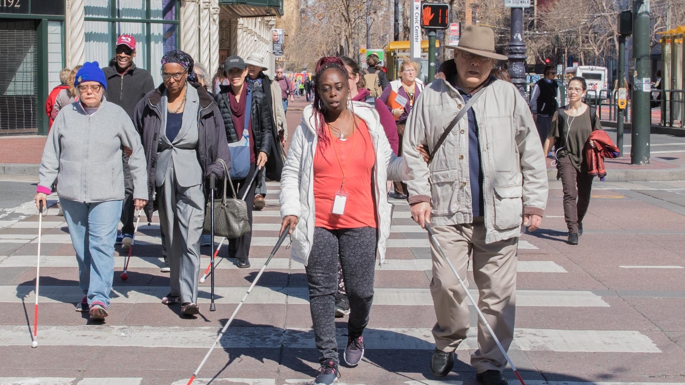 A group of people who are blind or have low vision using white canes walking in the crosswalk on Market Street in San Francisco