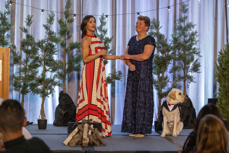 Keynote Speaker Rebecca Alexander and LightHouse CEO Sharon Giovinazzo stand together on stage - the stage is decorated with pine trmees and bistro lights to bring the essence of camp to the Grand Ballroo