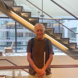 Robin Thiele, holding his white cane, stands in front of the internal staircase on the 10th floor of LightHouse headquarters
