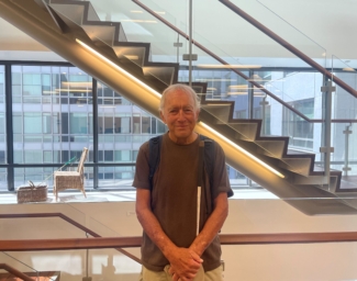 Robin Thiele, holding his white cane, stands in front of the internal staircase on the 10th floor of LightHouse headquarters