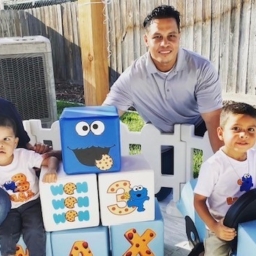 Mom, Dad, Sibling and Little Learner Max pose around Cookie Monster themed party decorations and blocks that say “MAX”