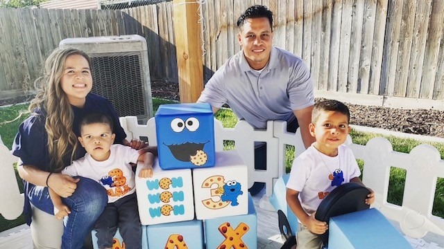 Mom, Dad, Sibling and Little Learner Max pose around Cookie Monster themed party decorations and blocks that say “MAX”