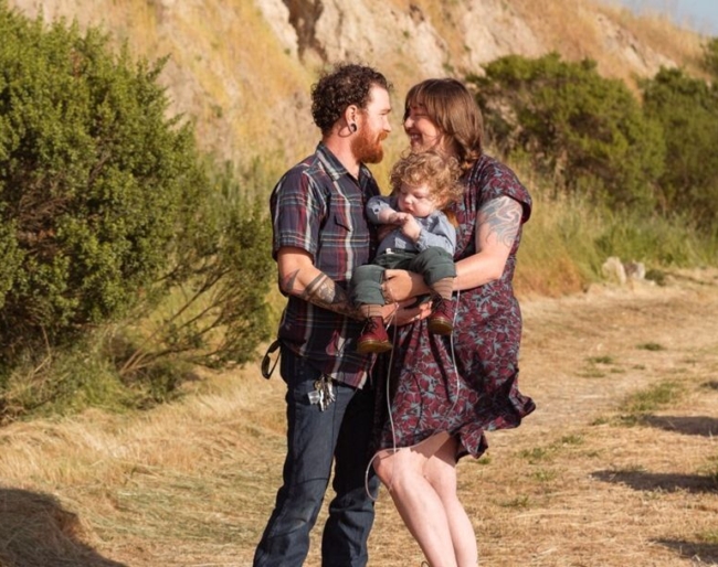 Little Learner parents hold they little learner while standing on a grassy hillside