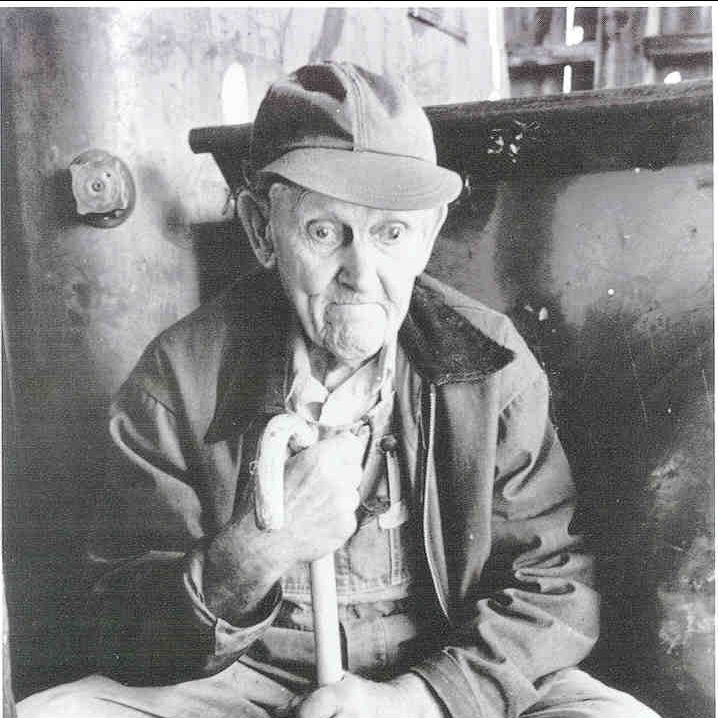 A black-nd-white photo of Earle Baum sitting and holding a cane with a curved top
