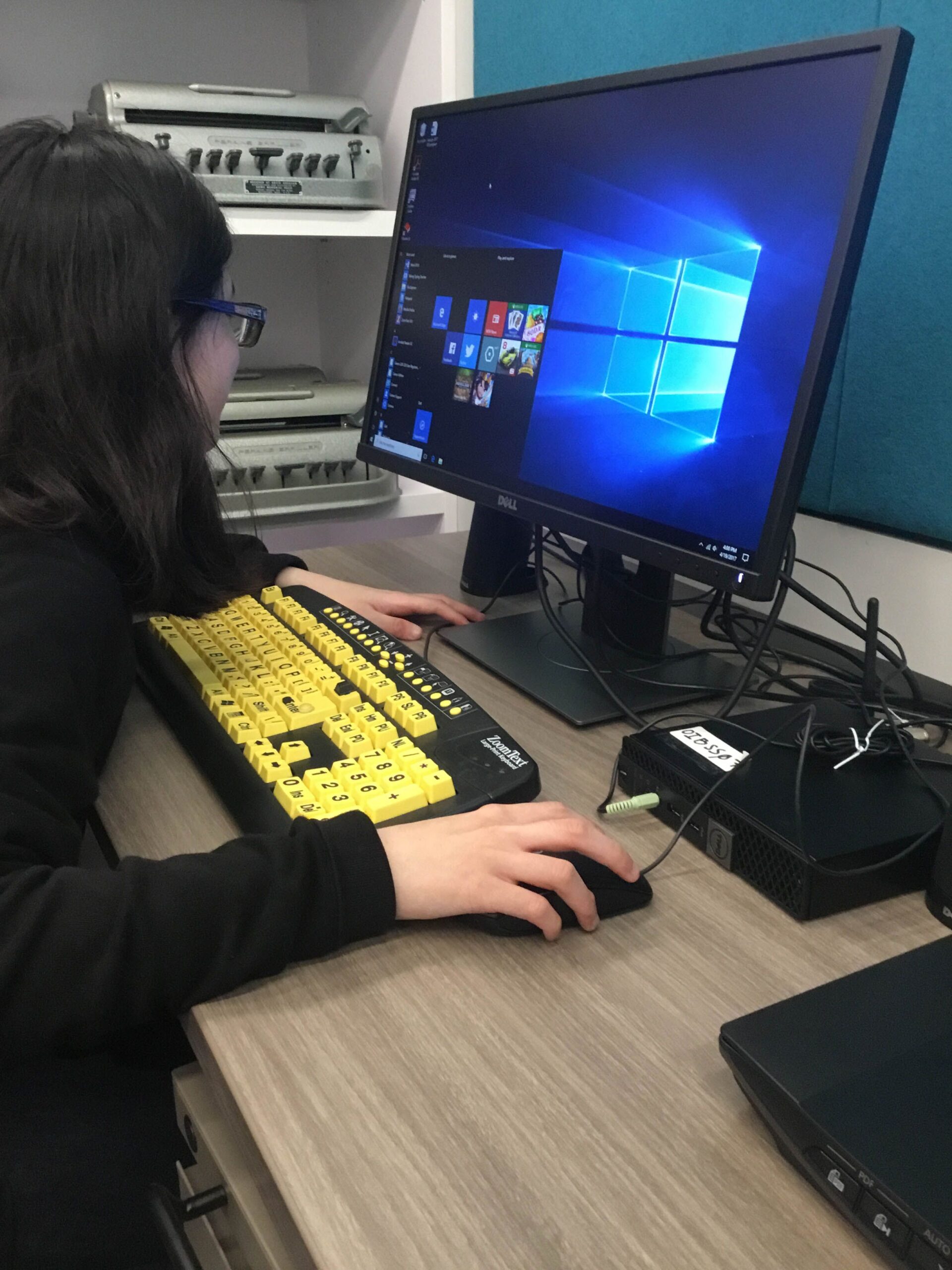  A student sits at a desktop computer with a large print keyboard with black on yellow keys
