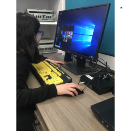 A student sits at a desktop computer with a large print keyboard with black on yellow keys