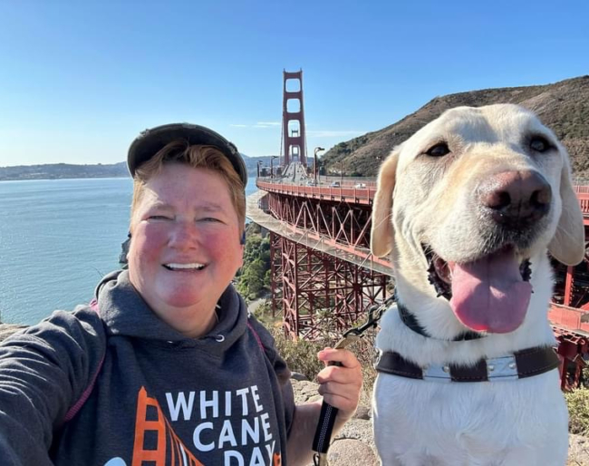 LightHouse CEO Sharon Giovinazzo and guide dog Pilot take a selfie with the bridge in the background.